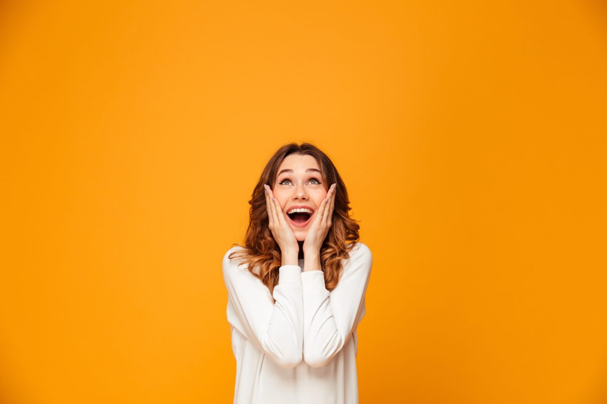 Surprised happy brunette woman in sweater holding her cheeks